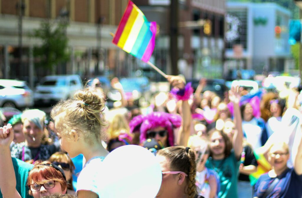 Multitud de personas durante la gay pride, resalta entre la multitud una persona disfrazada alzando la bandera del colectivo LGBTIQ+